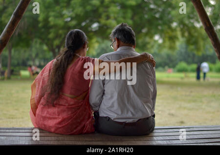 Senioren indische Frau liest aus Mobile und mit der Hand über die Schulter geschossen Ihres Mannes von hinten, während sie in einem Park in Neu Delhi sitzen Stockfoto