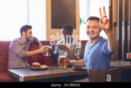 Aufgeregt, junger Kerl Bestellung mehr Bier, ruht mit Freunden an der Bar Stockfoto