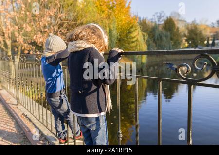 Kinder, Junge und Mädchen stehend rücken Brücke, an Enten, sonnigen Herbsttag im Park suchen, goldenen Stunde Stockfoto