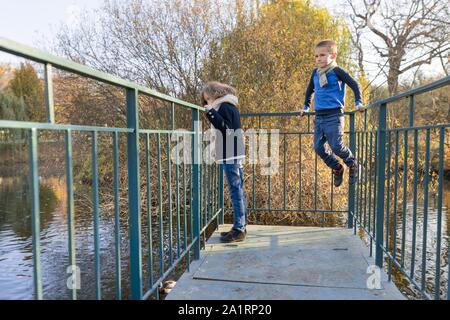 Kinder, Junge und Mädchen stehen auf Brücke, an Enten, sonnigen Herbsttag im Park suchen, goldenen Stunde Stockfoto