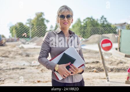 Portrait von Business reife Geschäftsfrau auf der Baustelle Instandsetzung der Straße in der Stadt, Pflasterstein Festlegung Stockfoto