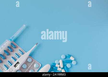 Behandlung von Erkältungen und Grippe. Verschiedene Medikamente, Thermometer, Sprays aus eine verstopfte Nase und ein Schmerz in einer Kehle auf blauem Hintergrund. Platz kopieren Stockfoto
