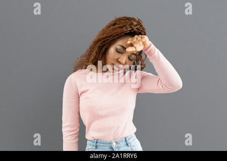 Erschöpft junge Mädchen ihre Stirn, grauen Hintergrund berühren Stockfoto