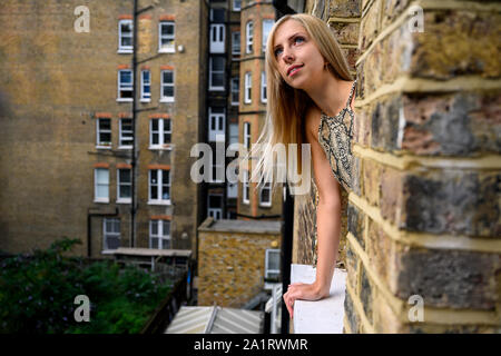 Porträt der jungen Frau mit Vertrauen in ihre Augen, Blick aus dem Fenster von einem alten Backsteingebäude und in der Hoffnung auf bessere Dinge in London zu kommen Stockfoto