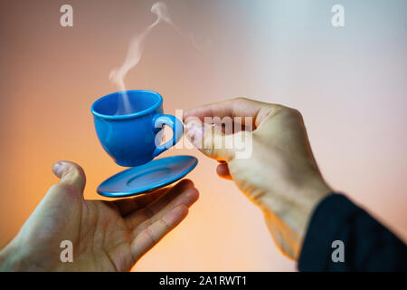 Floating blau Tasse Espresso mit Händen. First-Person anzeigen. Mock up des Segelfliegens in der Luft Tasse heißen Kaffee. Schweben Konzept Stockfoto