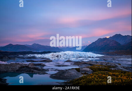 Wolken rosa und lila bei Sonnenuntergang über der Matanuska Gletscher in Alaska. Unter dem Gletscher eine ruhige See spiegelt die Farben und die Blätter haben begonnen, zu tu Stockfoto