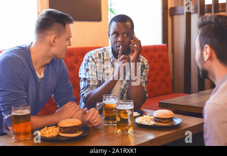 Afrikanischer Mann reden über Mobiltelefon, trinken Bier mit Freunden Stockfoto