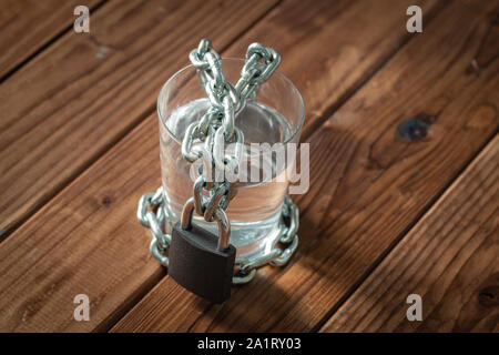 Ein Glas Wasser in einer Kette gewickelt und mit einem Vorhängeschloss. Das Konzept des Problem der kleinen Trinkwasser in der Welt. Stockfoto