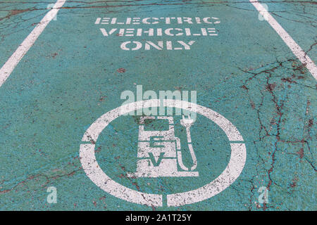 Parkplatz für Elektrofahrzeuge (EV) mit Symbol und Text „nur Elektrofahrzeuge“ auf alterndem grün lackiertem Straßenbelag. Stockfoto