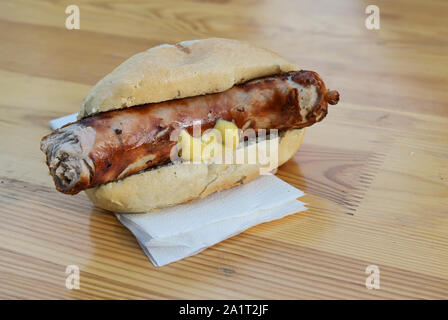 Bratwurst, in Deutschland als Bratwurst mit Senf in einem Brötchen auf einem Holztisch im Biergarten, Typisches Fast Food an deutschen Open Air Festival Stockfoto