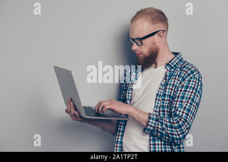 Portrait von attraktiven gut aussehender Mann in den beiläufigen kariertem Hemd Stil stilvolle Verschleiß auf hellgrauem Hintergrund mit Netbook Blick auf Monitor isoliert Stockfoto