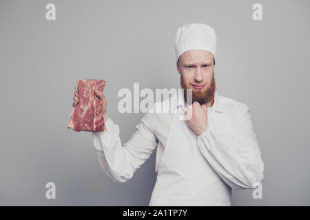 Portrait von er schön Gleichgesinnten attraktiv aussehenden Metzger guy Holding frisches Fleisch in arm Hand denken Wie zu kochen bereiten berühren Kinn Bart isoliert Stockfoto