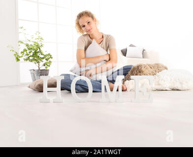 Home Konzepte, junge Frau umarmt eine grosse bequeme Kissen, sitzend auf dem Holzboden eines modernen Wohnzimmer mit Startseite Text, kopieren Raum Vorlage Stockfoto