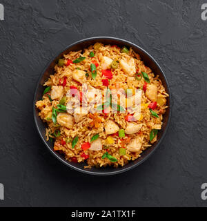 Schezwan Chicken Fried Rice in schwarz Schüssel am dunklen Schiefer Hintergrund. Szechuan Reis ist indo-chinesischen Küche Teller mit Paprika, Grüne Bohnen, Möhren, Stockfoto
