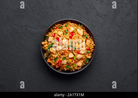 Schezwan Chicken Fried Rice in schwarz Schüssel am dunklen Schiefer Hintergrund. Szechuan Reis ist indo-chinesischen Küche Teller mit Paprika, Grüne Bohnen, Möhren, Stockfoto