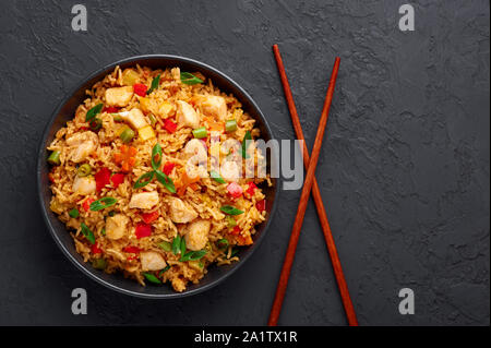 Schezwan Chicken Fried Rice in schwarz Schüssel am dunklen Schiefer Hintergrund. Szechuan Reis ist indo-chinesischen Küche Teller mit Paprika, Grüne Bohnen, Möhren, Stockfoto