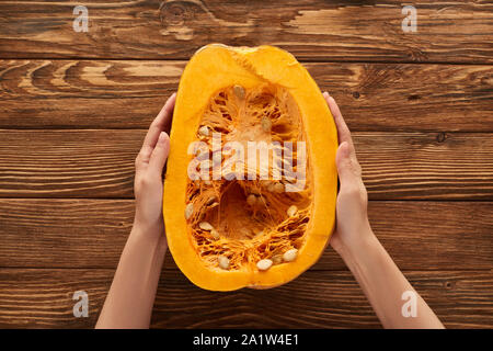 7/8-Ansicht von Frau mit der Hälfte der Kürbis auf braunem Holz- Oberfläche Stockfoto