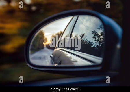 Reflexion der weg in den Sonnenuntergang Sonne verschwommen in die Außenspiegel des Autos. Close-up Stockfoto