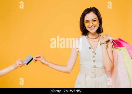 Happy girl in Sonnenbrille mit Einkaufstaschen, die Kreditkarte isoliert auf Gelb Stockfoto