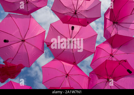 Zwei Reihen von bunten hellen rosa Sonnenschirme gegen einen bewölkten Himmel bis auf die Griffe von unten Stockfoto