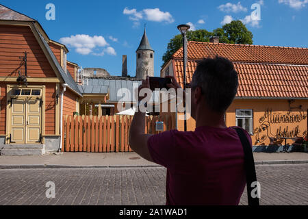 Rückansicht des Menschen ein Bild von Haapsalu Schloss und historischen Gebäuden mit Handy beim Stehen auf karja Street, Haapsalu, Estland, Balti Stockfoto