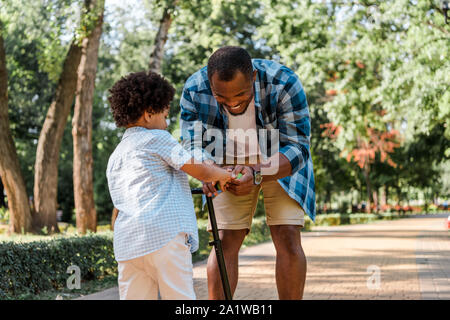 Happy african american Vater steht in der Nähe von Son und Scooter Stockfoto