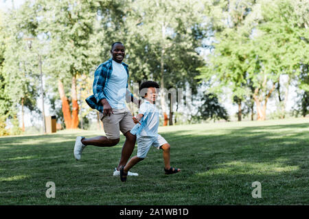 Happy african american Vater und Sohn, die auf Gras Stockfoto