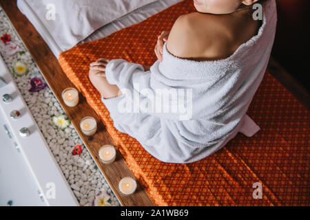 7/8-Ansicht von Frau im Bademantel saß auf Massage Matte in Spa Salon Stockfoto