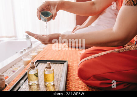 7/8-Ansicht von Masseur gießen Duft Öl auf der Hand Stockfoto