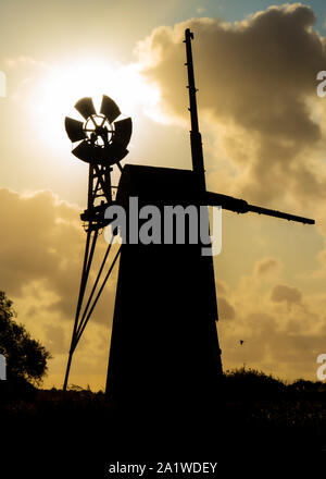 Rasen Fenn Entwässerung Mühle aus über den Fluss als Silhouette mit der Sonne hinter sich. Stockfoto