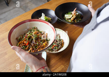 Nahaufnahme des unkenntlich Kellner Holding zwei Platten mit köstlichen asiatischen Gerichte, während Sie im Café oder Restaurant, kopieren Raum Stockfoto