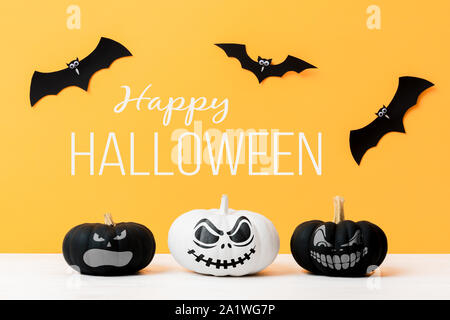 Drei unheimlichen, schwarzen und weißen Jack o Laternen und fliegende Papier Fledermäuse auf gelben Hintergrund. Halloween Hintergrund. Stockfoto