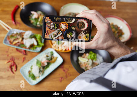 Nahaufnahme des unkenntlich Mann, Foto, köstliche asiatische Lebensmittel auf hölzernen Tisch im Café oder Restaurant, der Bildschirm des Smartphones konzentrieren, kopieren Raum Stockfoto