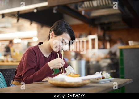 Portrait von lächelnden jungen Frau genießen Sie köstliche Speisen, während bei Tisch in den asiatischen Cafe oder Restaurant sitzen, Platz kopieren Stockfoto