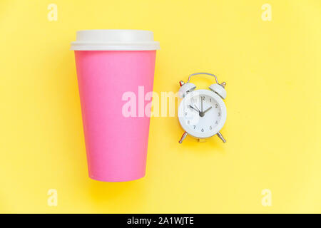 Einfach flach Design rosa Papier Kaffeetasse und Wecker auf Gelb bunte trendy Hintergrund isoliert. Takeaway trinken Frühstück trinken. Guten Morgen aufwachen wach Konzept. Ansicht von oben kopieren Raum Stockfoto