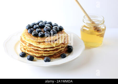 Stapel Pfannkuchen mit Honig und Blaubeeren mit Puderzucker bestäubt auf weißem Hintergrund Stockfoto