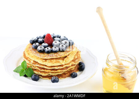 Stapel Pfannkuchen mit Honig, Blaubeeren und roten Himbeeren bestäubt mit Puderzucker auf weißem Hintergrund Stockfoto