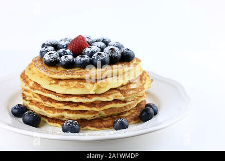 Stapel Pfannkuchen mit Honig, Blaubeeren und roten Himbeeren bestäubt mit Puderzucker auf weißem Hintergrund Stockfoto