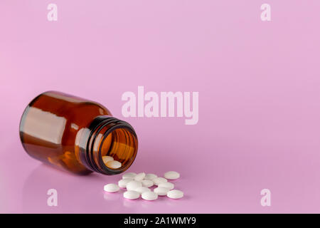 Weiße, runde Tabletten vor Glas Flasche Pillen verstreut Stockfoto