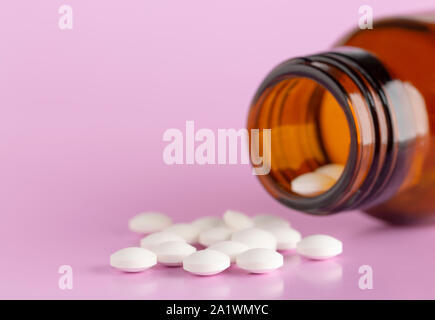 Weiße, runde Tabletten vor Glas Flasche Pillen verstreut Stockfoto