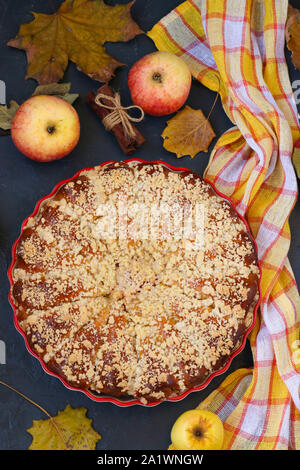 Torte mit Äpfeln wird in eine keramische Form auf einem dunklen Hintergrund, Ansicht von oben entfernt, vertikale Ausrichtung Stockfoto