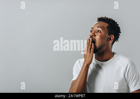 Schockiert afrikanische amerikanische Mann im weißen T-Short für den Mund mit der Hand und die Kamera isoliert auf Grau Stockfoto