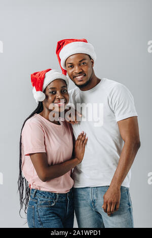 Afrikanische amerikanische Ehepaar in Santa Hüte an Kamera isoliert auf Grau suchen Stockfoto