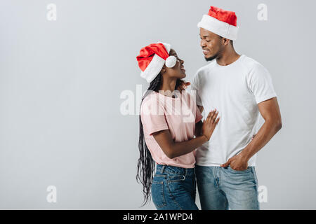 Afrikanische amerikanische Ehepaar in Santa Hüte an einander Suchen isoliert auf Grau Stockfoto