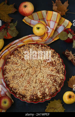 Torte mit Äpfeln wird in eine keramische Form auf einem dunklen Hintergrund, Ansicht von oben entfernt, vertikale Ausrichtung Stockfoto