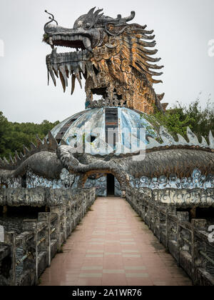 Riesig und unheimlich stone Dragon mit Spikes und offener Mund mit Zähnen in der Seitenansicht mit Fußweg an verlassenen Water Park, Thuy Tien See, Hue, Vietnam Stockfoto