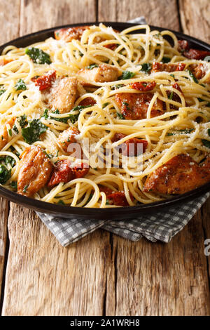 Leckere Spaghetti mit Fried Chicken, getrockneten Tomaten und Spinat close-up auf einem Teller auf den Tisch. Vertikale Stockfoto