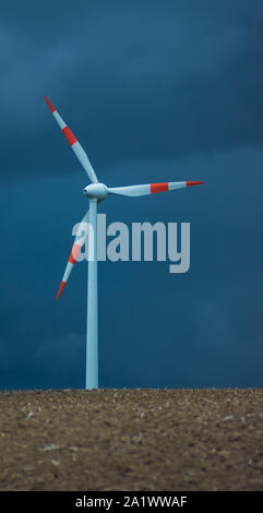 Windkraftanlage vor gewitterwolken auf kargen Feld im Herbst Stockfoto