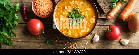 Rote Linsensuppe auf hölzernen Hintergrund, Ansicht von oben, Banner. Traditionelle türkische oder arabische Linsen und Gemüse würzige Suppe, gesunde vegane Ernährung. Stockfoto