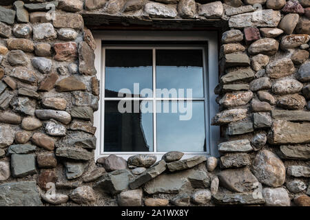 Natursteinmauer mit bunten und unterschiedlich großen Steinen und Fenster Stockfoto